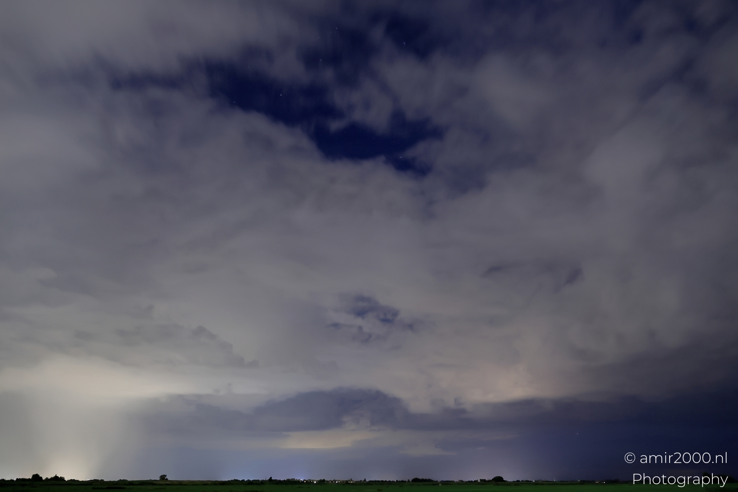 Moonlit storm base over Noord-Holland fields with faint stars and small village lights visible.
