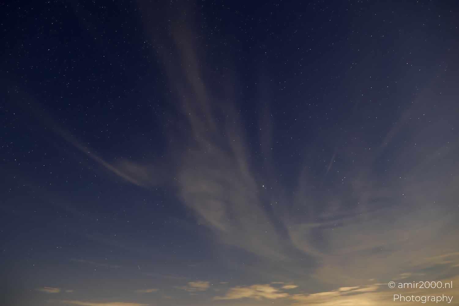 Radiating cloud textures between stars with subtle blue gradient and soft town glow on horizon.