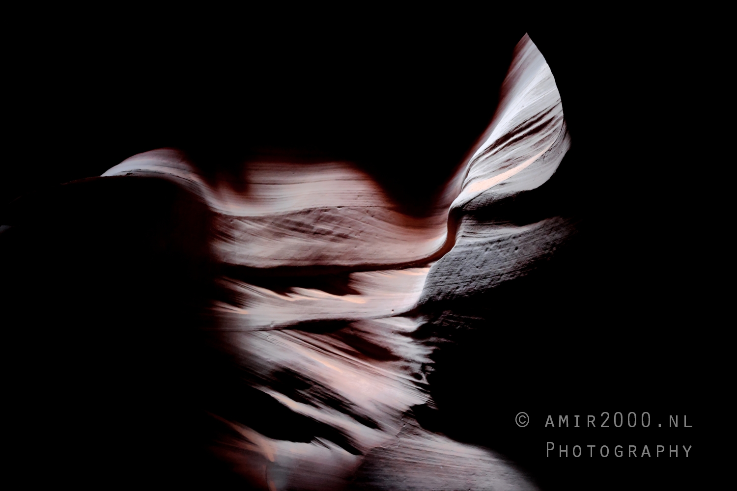 Abstract sandstone curves in deep shadow with narrow slit of glowing light at Antelope Canyon