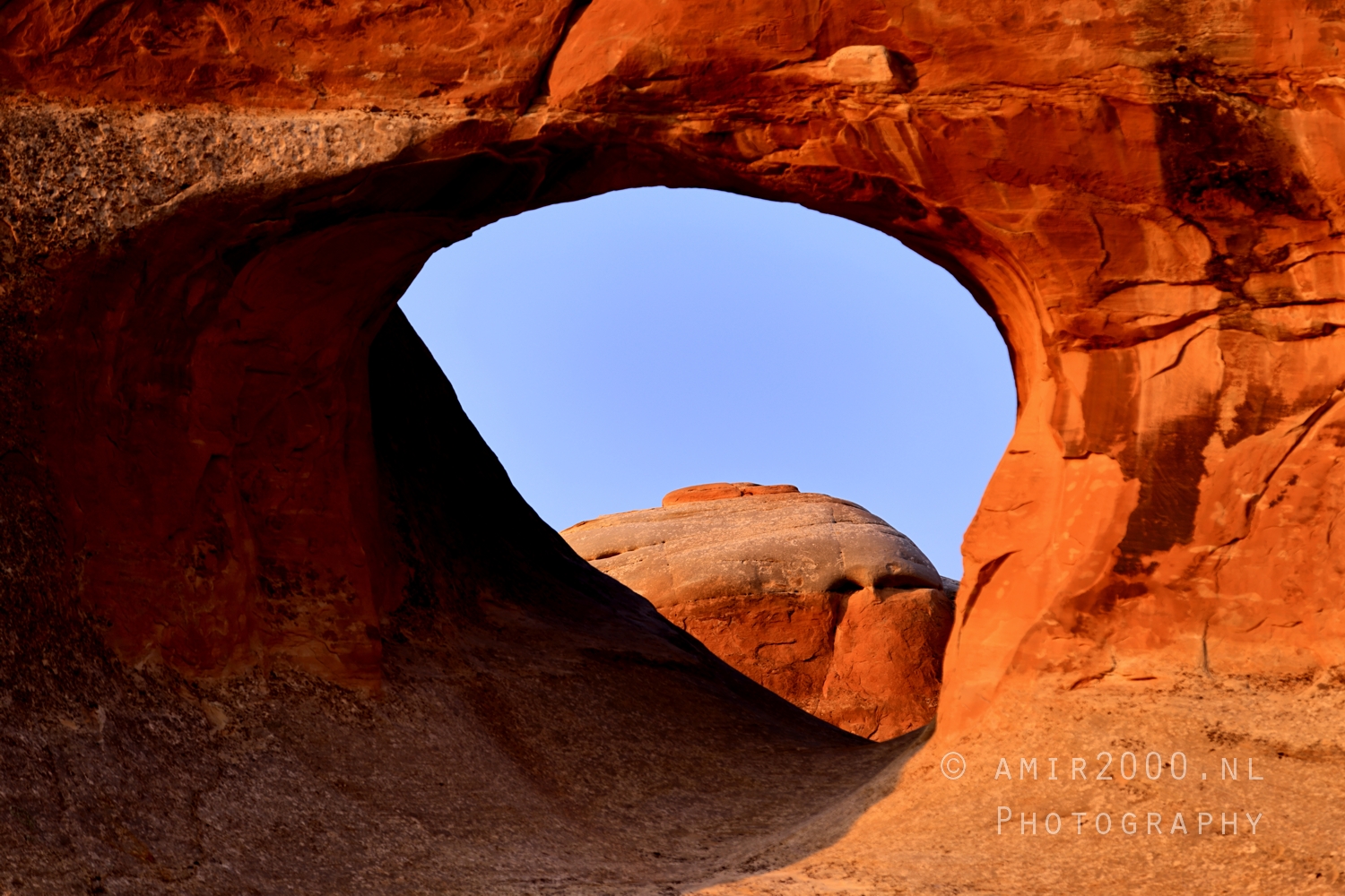 Rounded butte centered inside the arch opening at sunset with warm red light