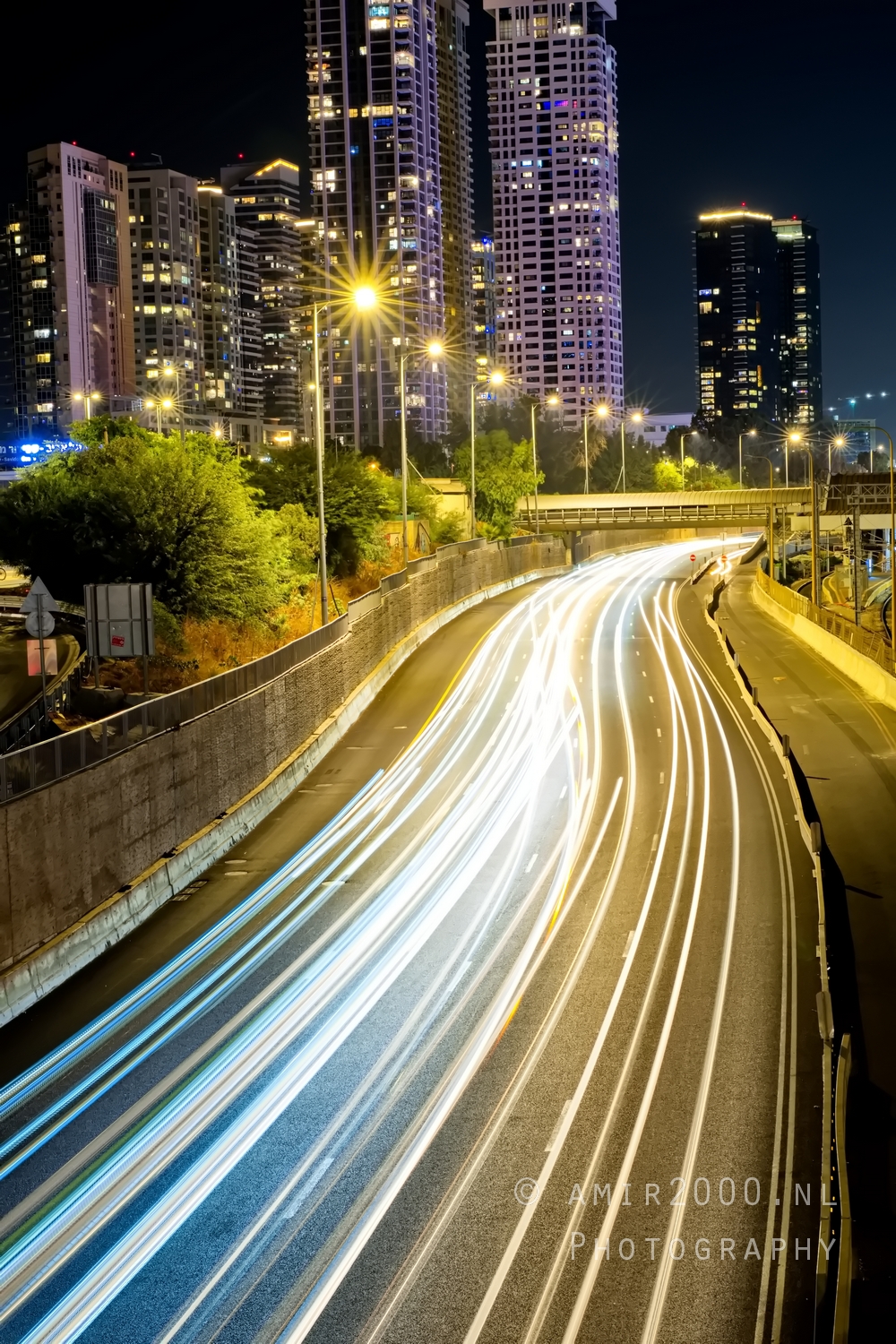 Tall vertical view of curved highway with bright light trails and high rises