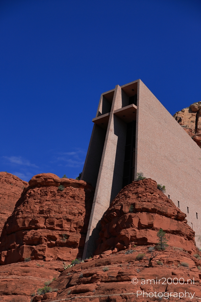 Side view of the chapel rising above red rock, hard sun and deep shadow.