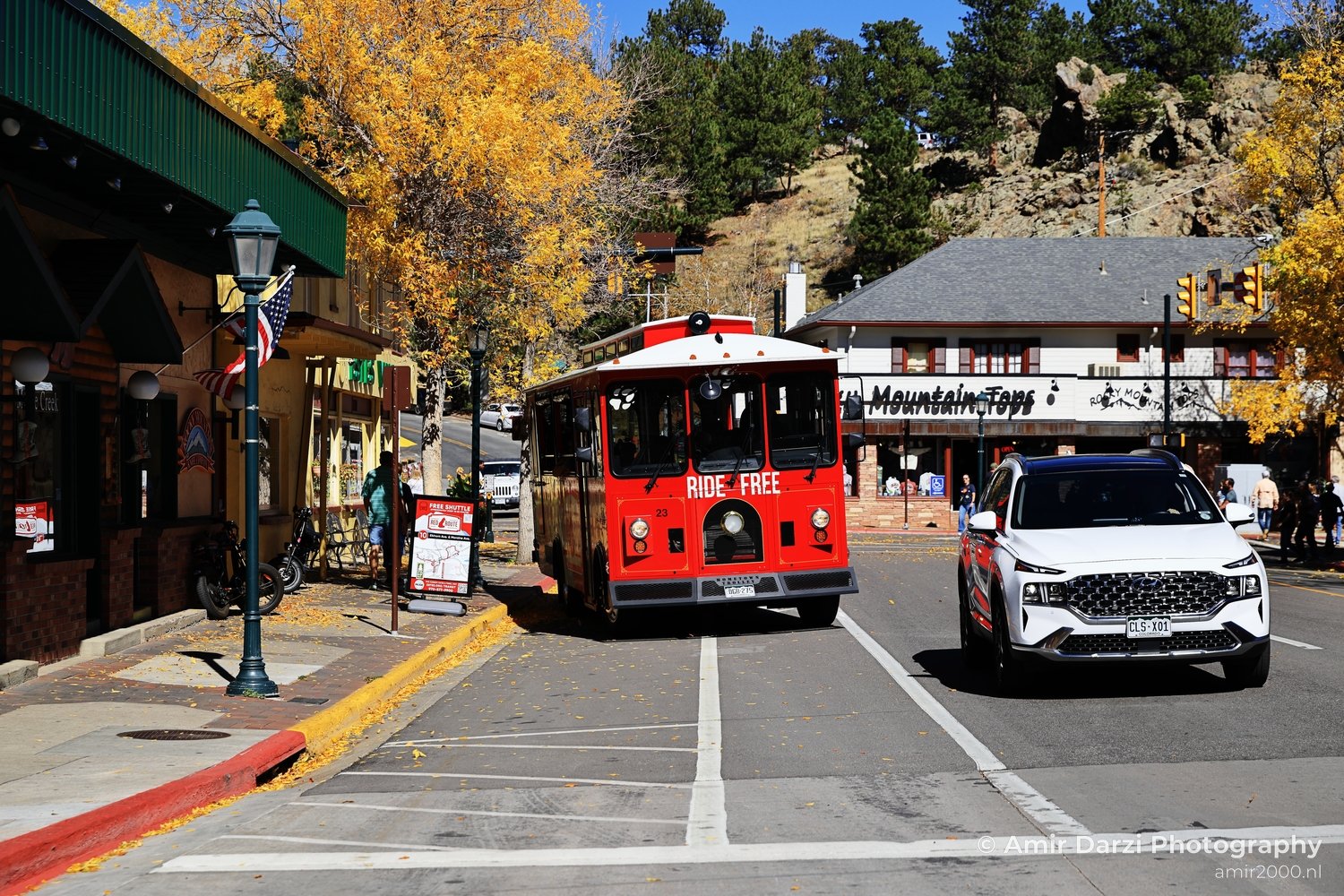 Red vintage-style trolley with 'RIDE FREE' sign next to a white contemporary vehicle amidst golden trees.