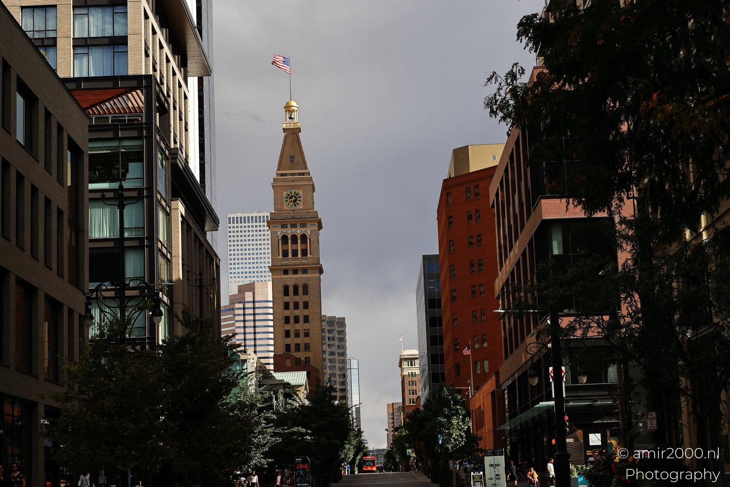 A prominent clock tower with an American flag stands in the urban landscape of downtown Denver.