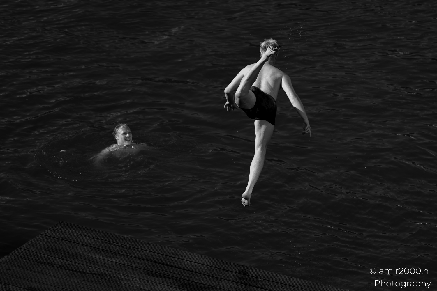 Takeoff from wooden deck into an Amsterdam canal as a swimmer watches, black and white