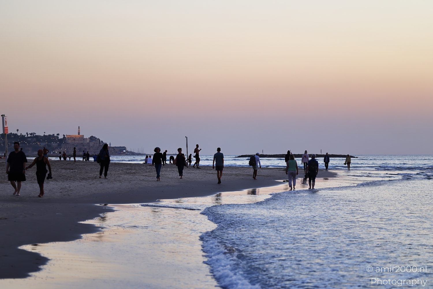 People walking near the shoreline as evening light reflects on the water