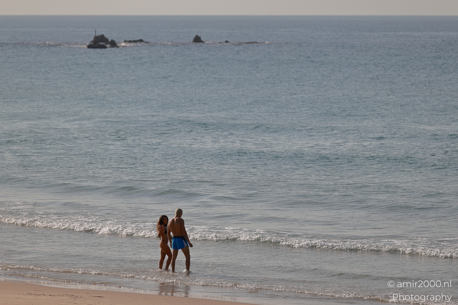 Two swimmers standing together at the edge of gentle incoming waves