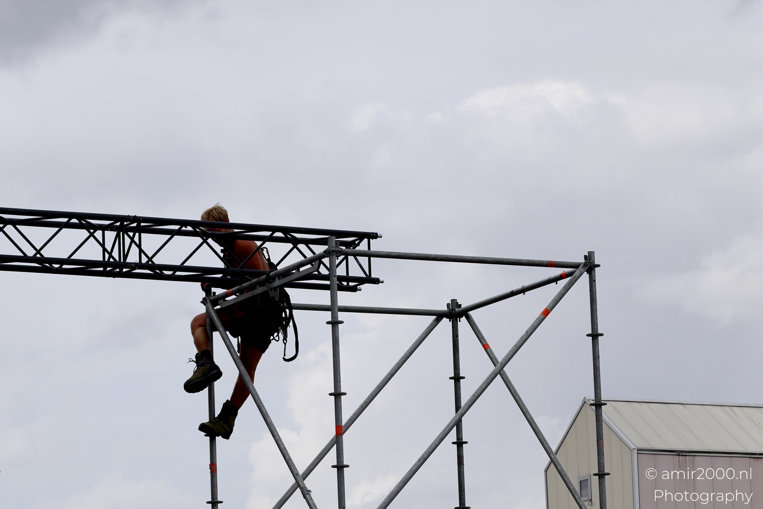 Rigger locking truss to scaffold in Amsterdam, repeating windows behind, quiet daylight and steady hands at the junction.