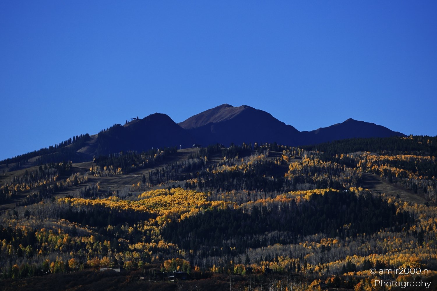 Vibrant fall foliage adorns the mountains against a bright azure backdrop.