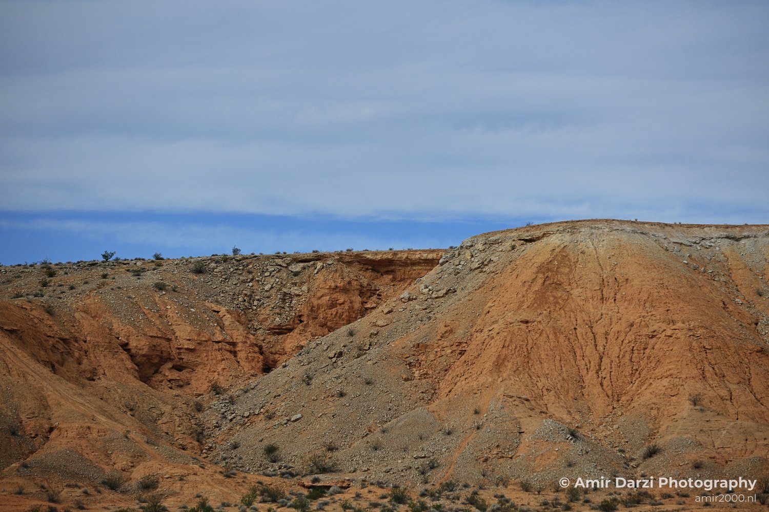 A dry and desolate desert environment featuring rocky hills under a cloudy sky.