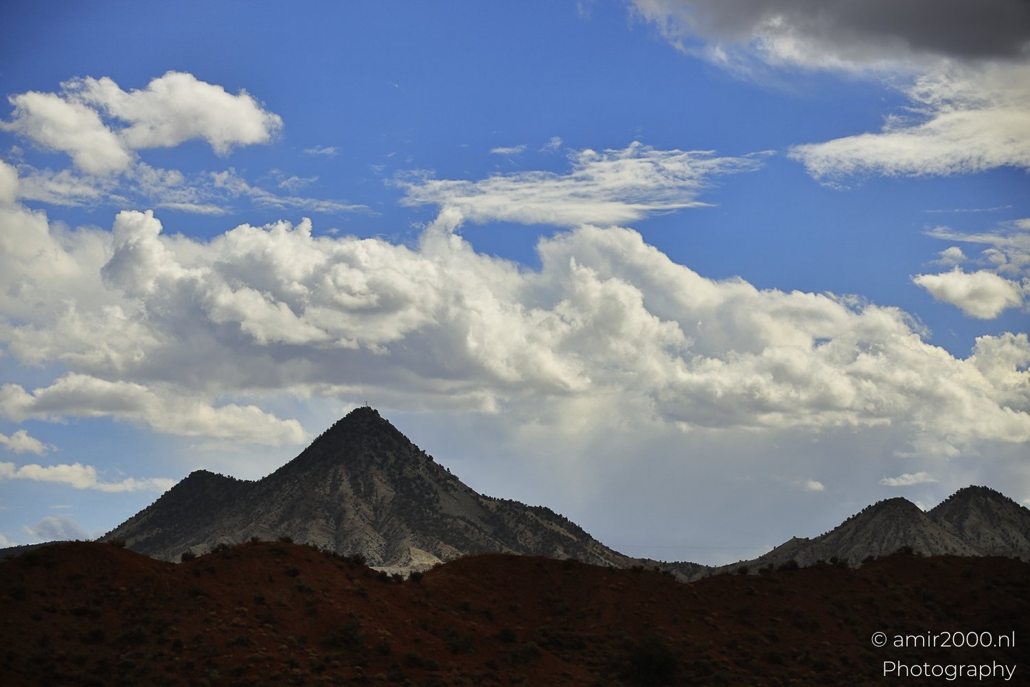 Desert scenery featuring prominent butte with scattered clouds above it.