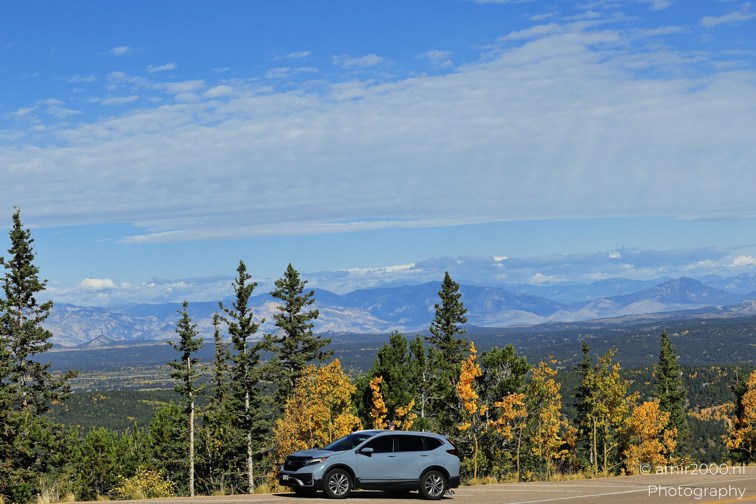 Overlook with parked silver SUV and golden aspens, wide view, bright morning light, cloud shelf above.