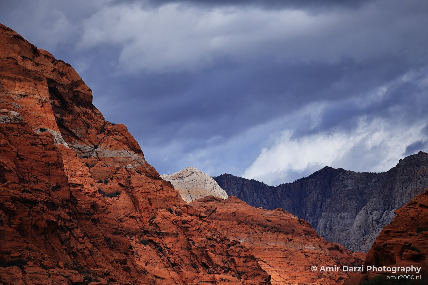 A close-up view of red sandstone formations with dark clouds above them and sparse vegetation on the ground.