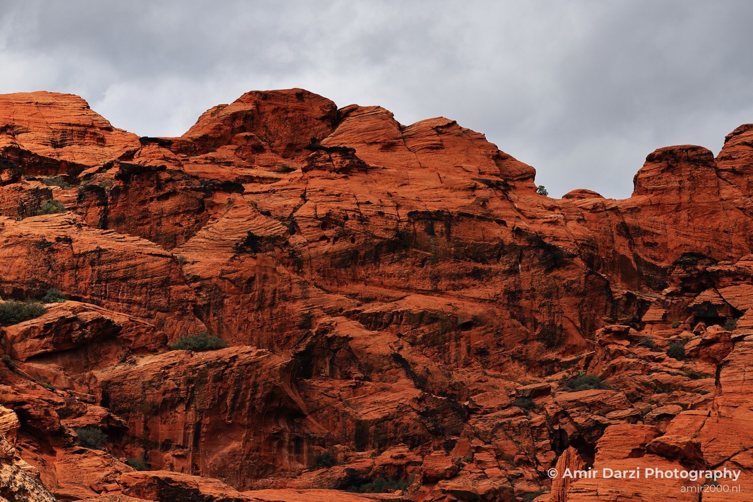 A striking view of layered red rock strata in a desert landscape with sparse vegetation and cloudy skies.