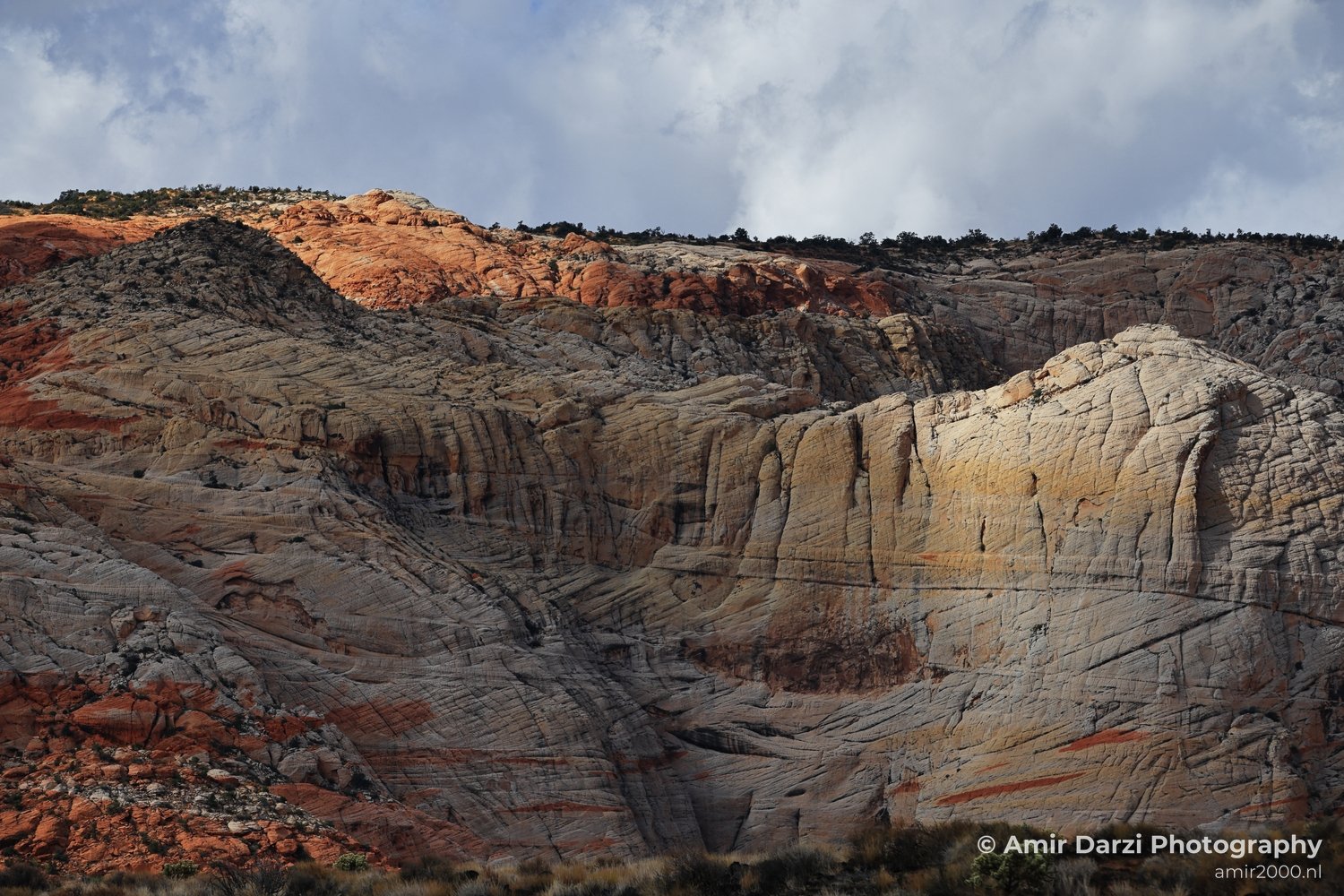 Red rock formations with sparse vegetation below and a cloudy sky above.
