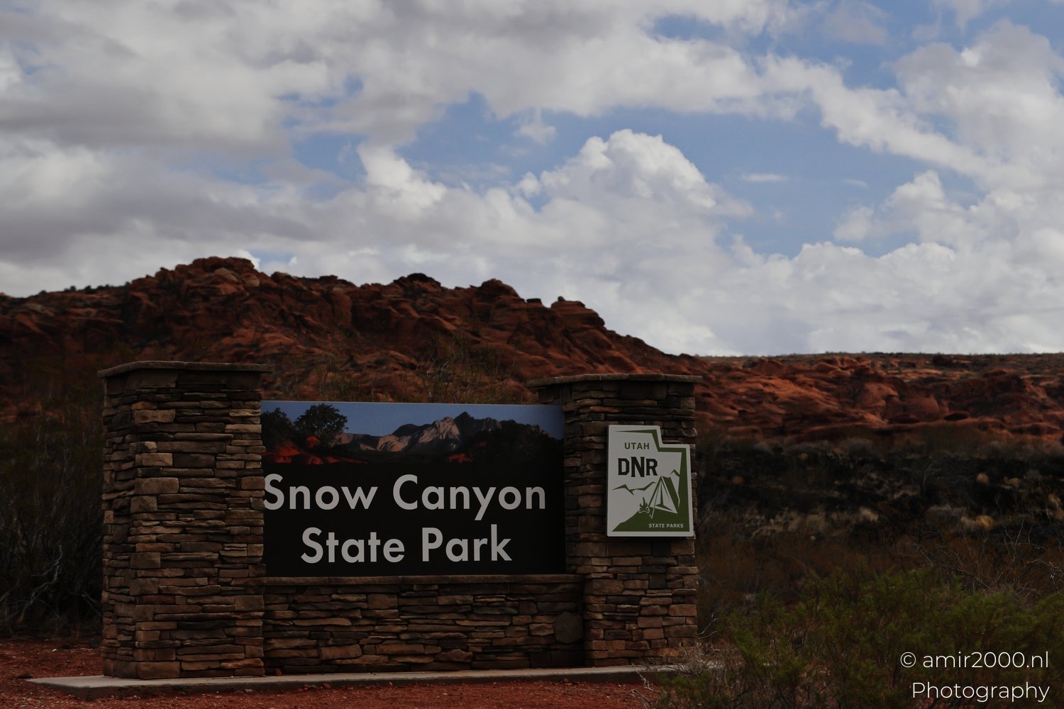 A sign for the park with red rock formations and desert vegetation in the background.