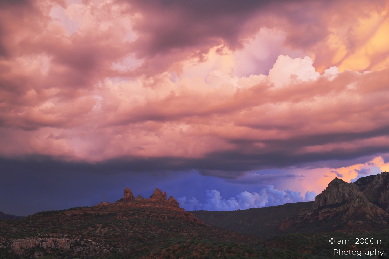 Rugged Sedona mountains from distance, warm light on rock faces, misty rain veil at left.