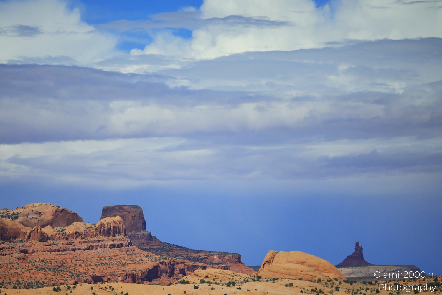 Distant desert buttes from a moving car, under stacked clouds with a bright blue opening.