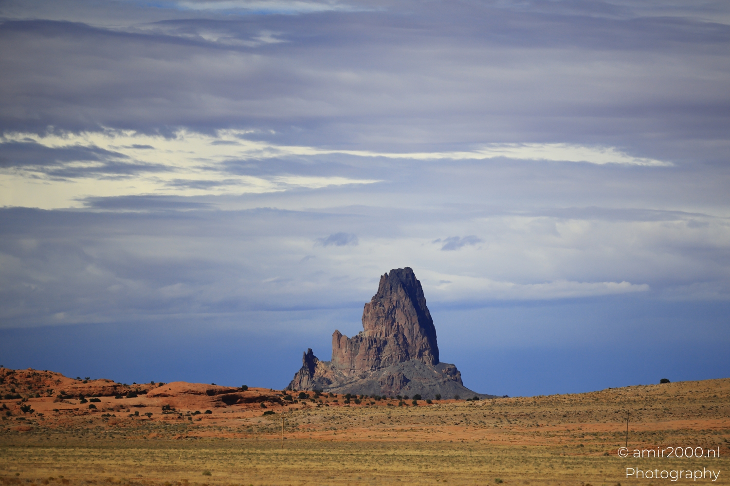 Church Rock spire centered from roadside perspective, with red rock band and soft layered cloud ceiling.