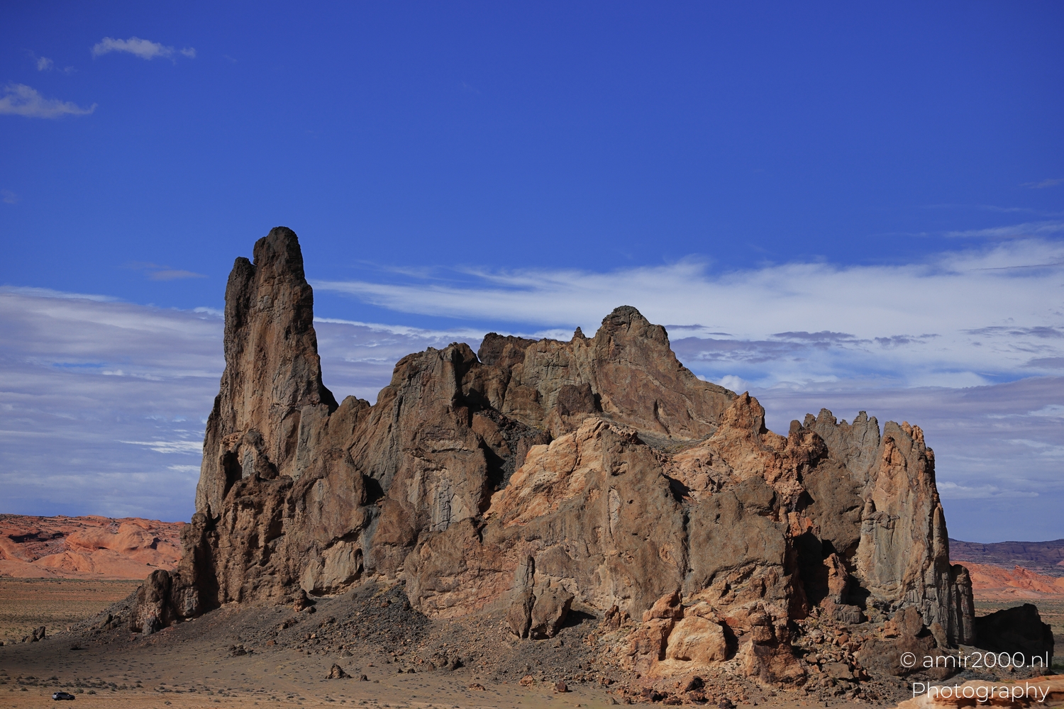Large rugged rock outcrop from roadside view, side lit in warm sun under a clear blue sky.