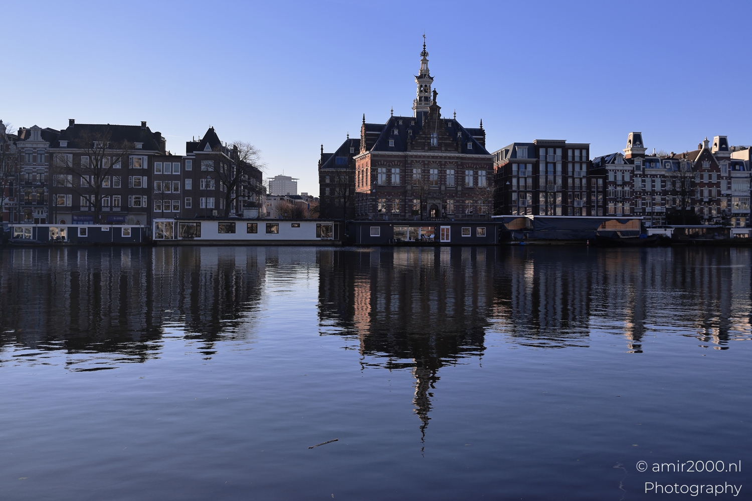 Historic riverside building reflected in calm blue water under bright winter morning light
