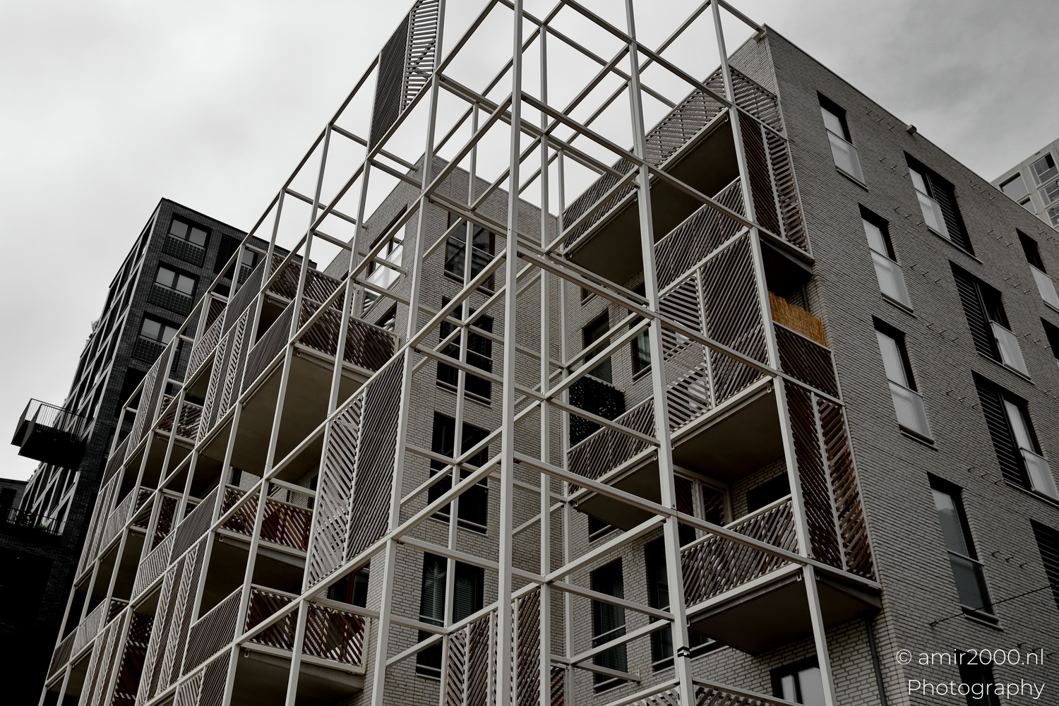 White lattice balconies and slatted panels at Amsterdam Sloterdijk housing block, oblique view under overcast light.