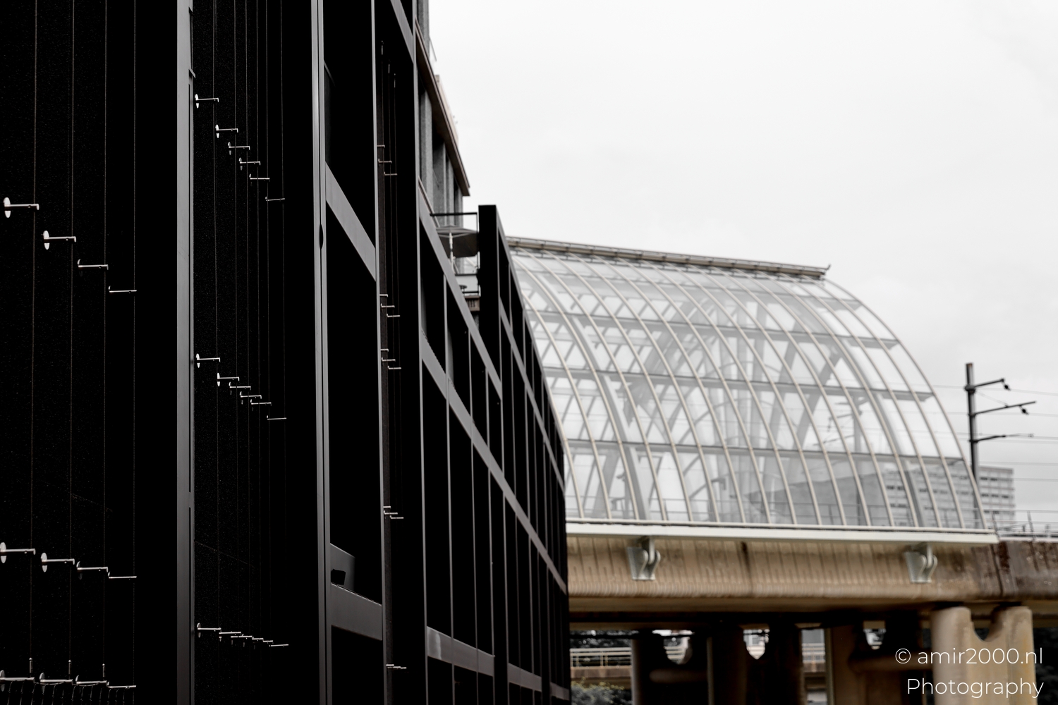 Sloterdijk station glass arc and black residential block against blank sky, soft grey daylight.