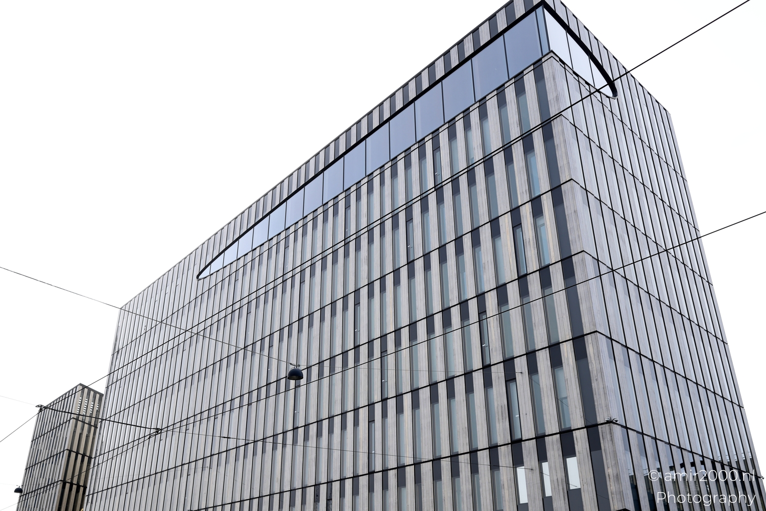 Upward view of vertical timber cladding and glass windows in calm grey daylight near the harbor.