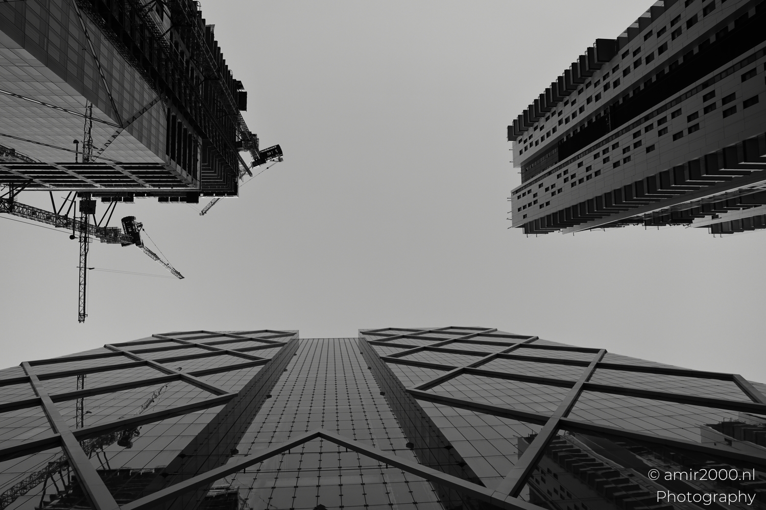 Three high rises frame open sky, centered glass grid, edge cranes, low angle dusk.