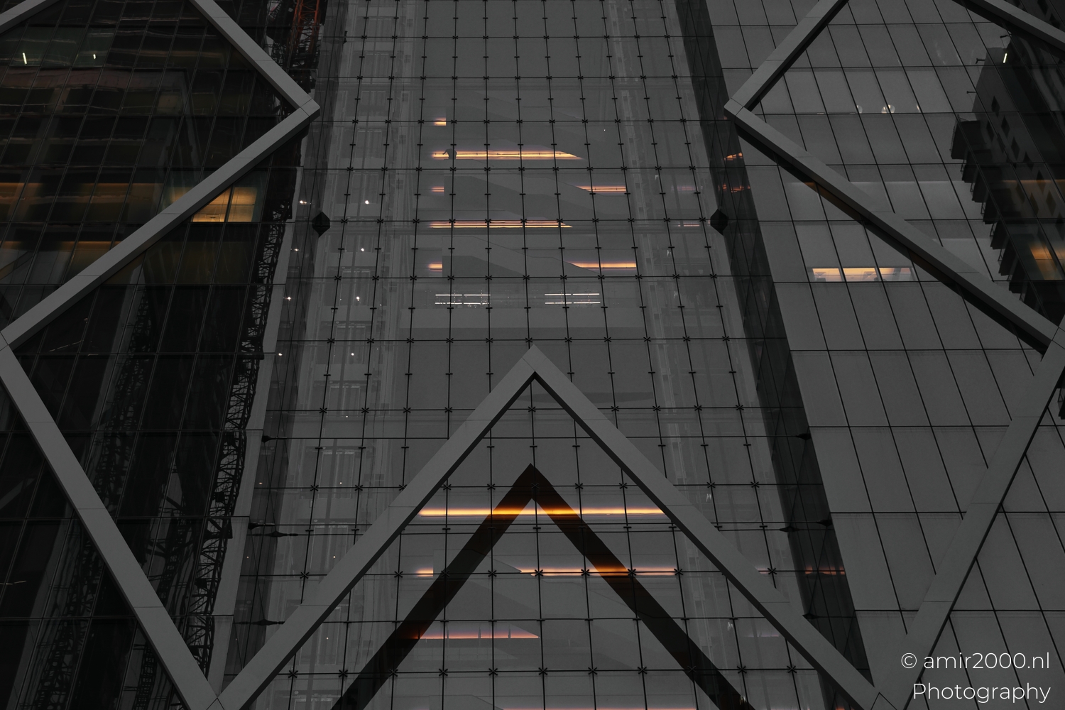 Facade bracing frames warm interior light bars, close upward view through dark reflective glass.