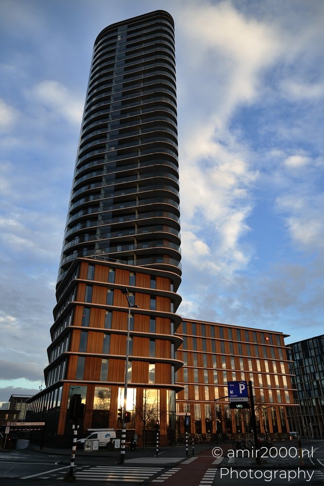 The MEININGER Hotel Amstel Skyscraper stands tall under a cloudy sky backdrop.