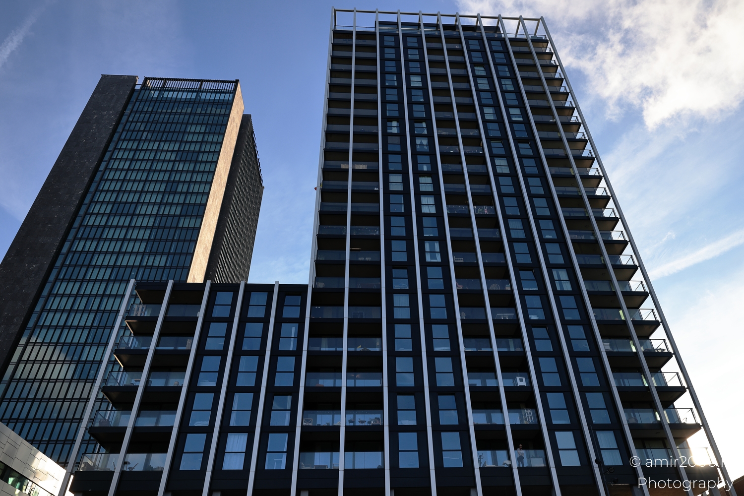 Curving residential tower facade photographed upward with dark windows and pale blue sky