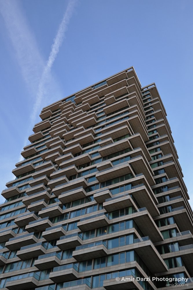 Contemporary skyscraper adorned with balconies and glass windows against clear blue sky.