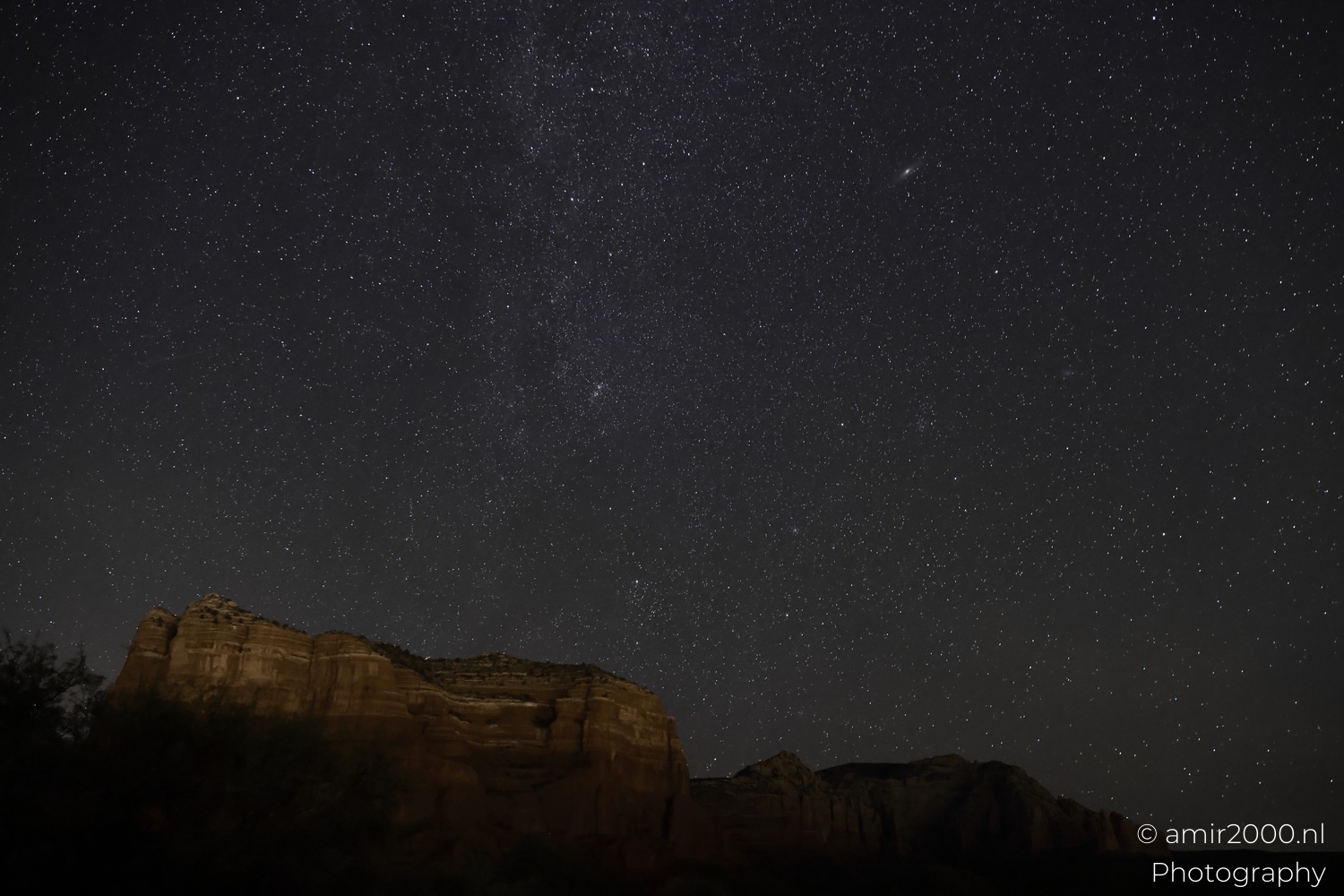 Bell Rock ridge line under dense stars, low horizon glow behind, wide night landscape framing