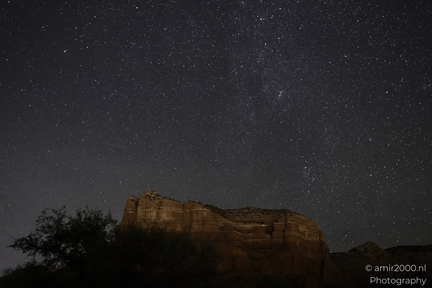 Starry sky with faint Milky Way texture above Bell Rock forms, gentle horizon glow, wide view