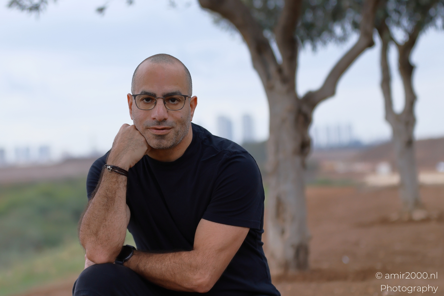 Tighter self portrait in Ariel Sharon Park, balanced tones, calm expression, soft tree background.
