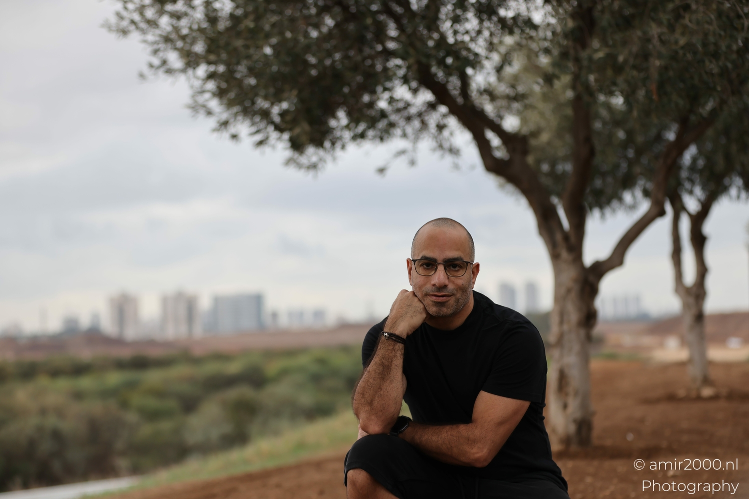 Self portrait seated in Ariel Sharon Park, soft morning light, trees and distant skyline blur.