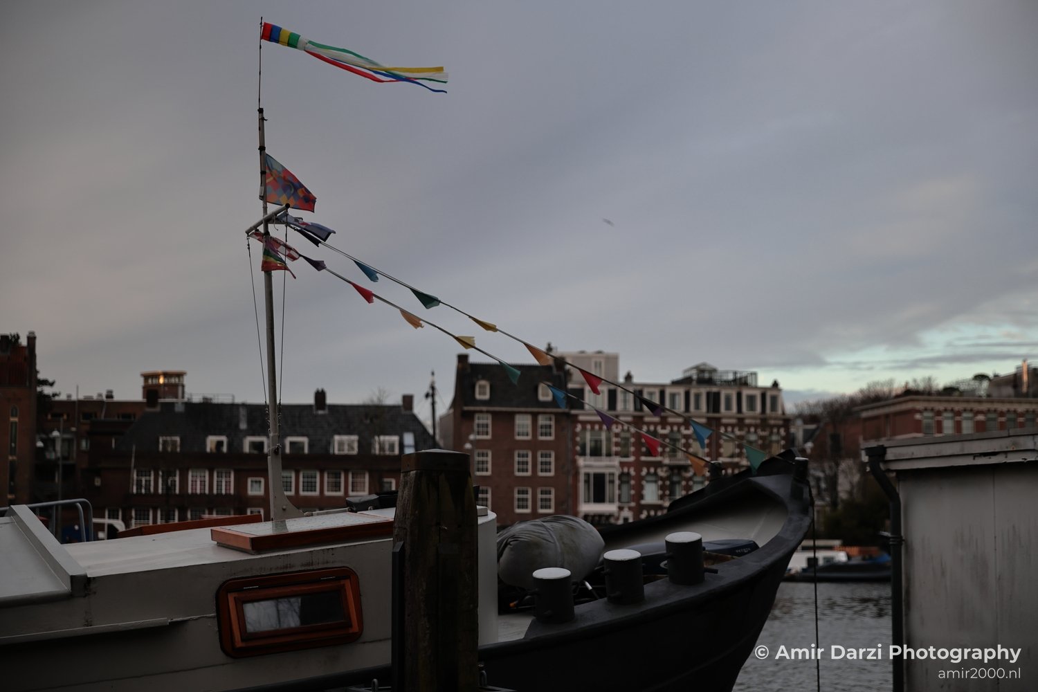 Cloudy-day view of an ornately decorated vessel by canalfront buildings and residences.