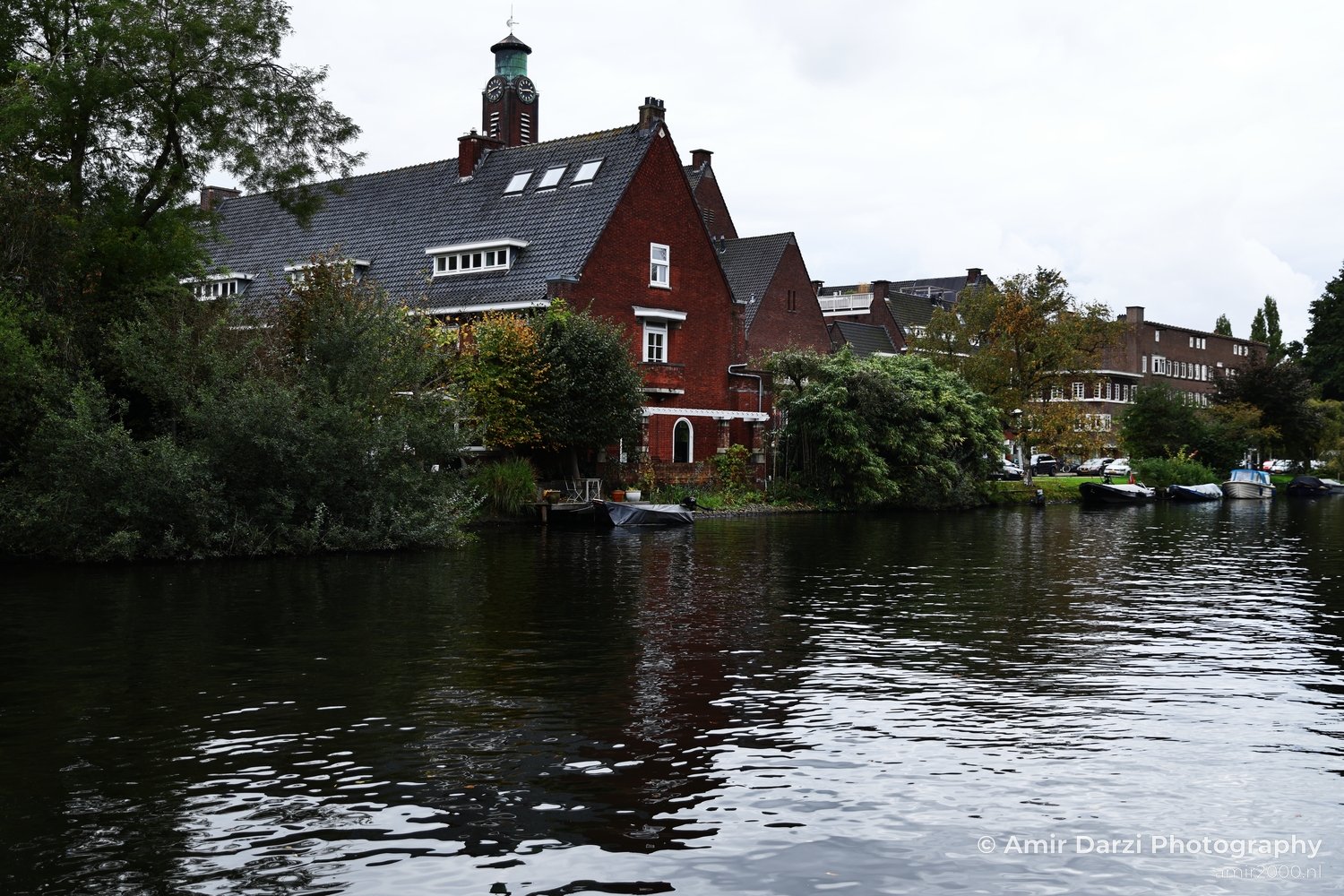 A tranquil canal mirrors historic architecture and parked cars near Zuid Autumn foliage adds color to the scene.