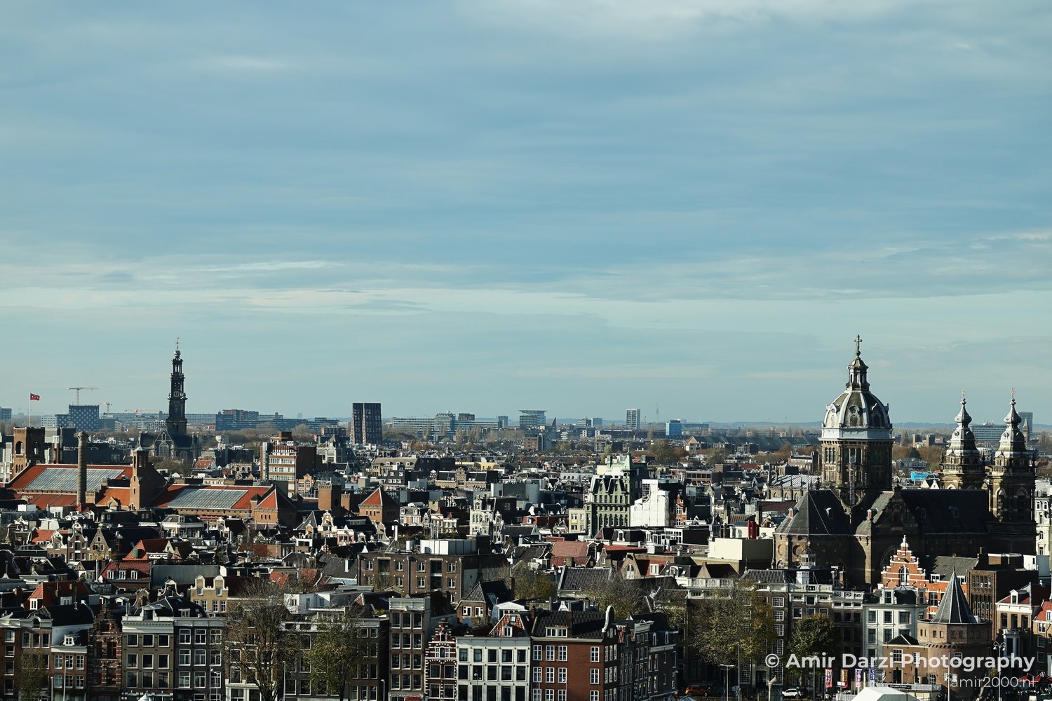 An aerial cityscape with traditional Dutch rooftops in the foreground and modern structures extending into the horizon.