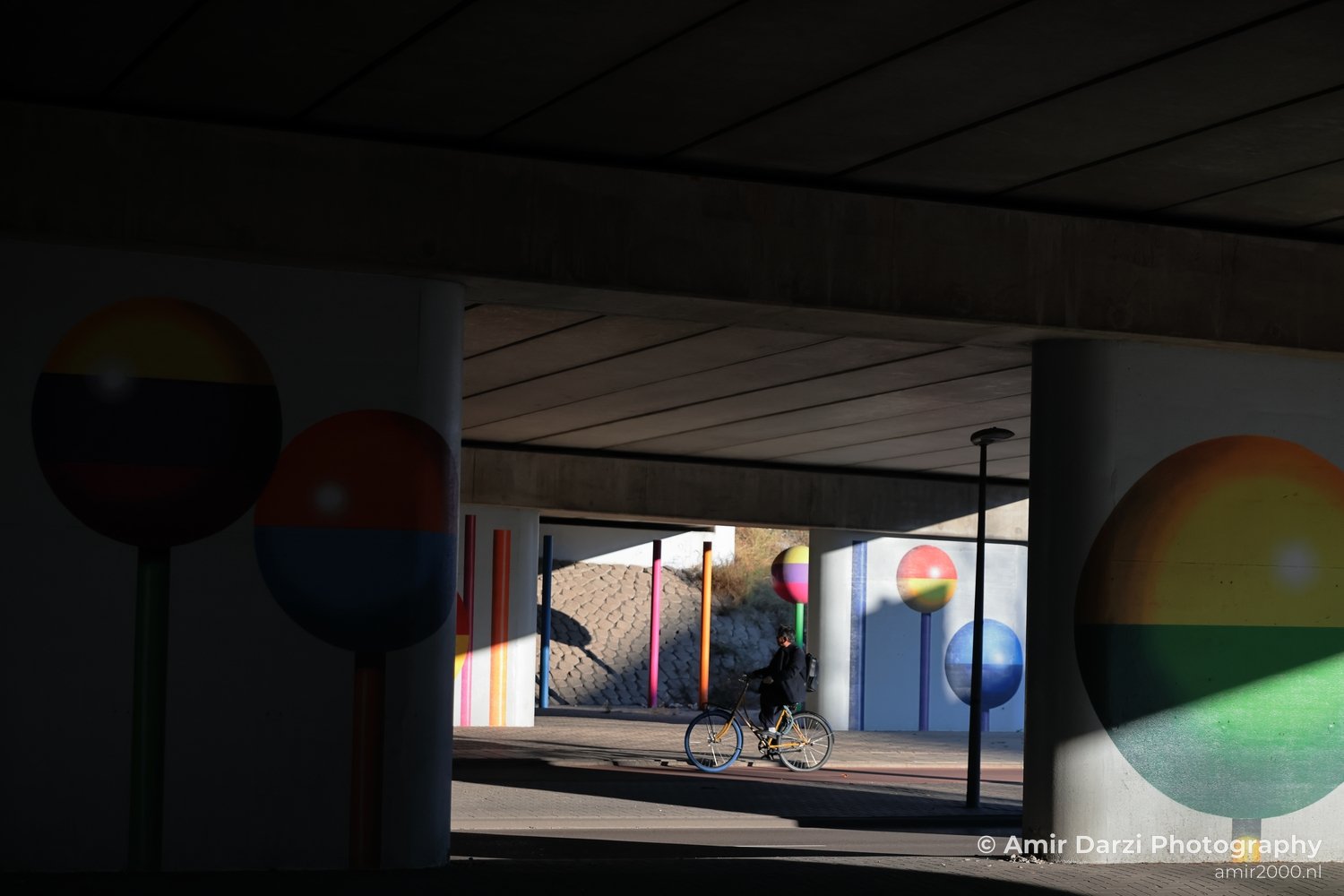 Cyclist passing through an urban art installation featuring colorful balloons on concrete pillars in Amsterdam Netherlands.