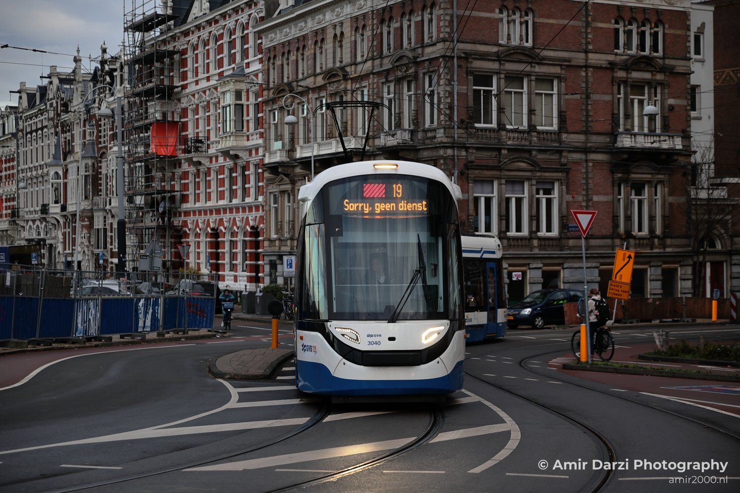 Modern electric tram on city streets near red brick architecture.
