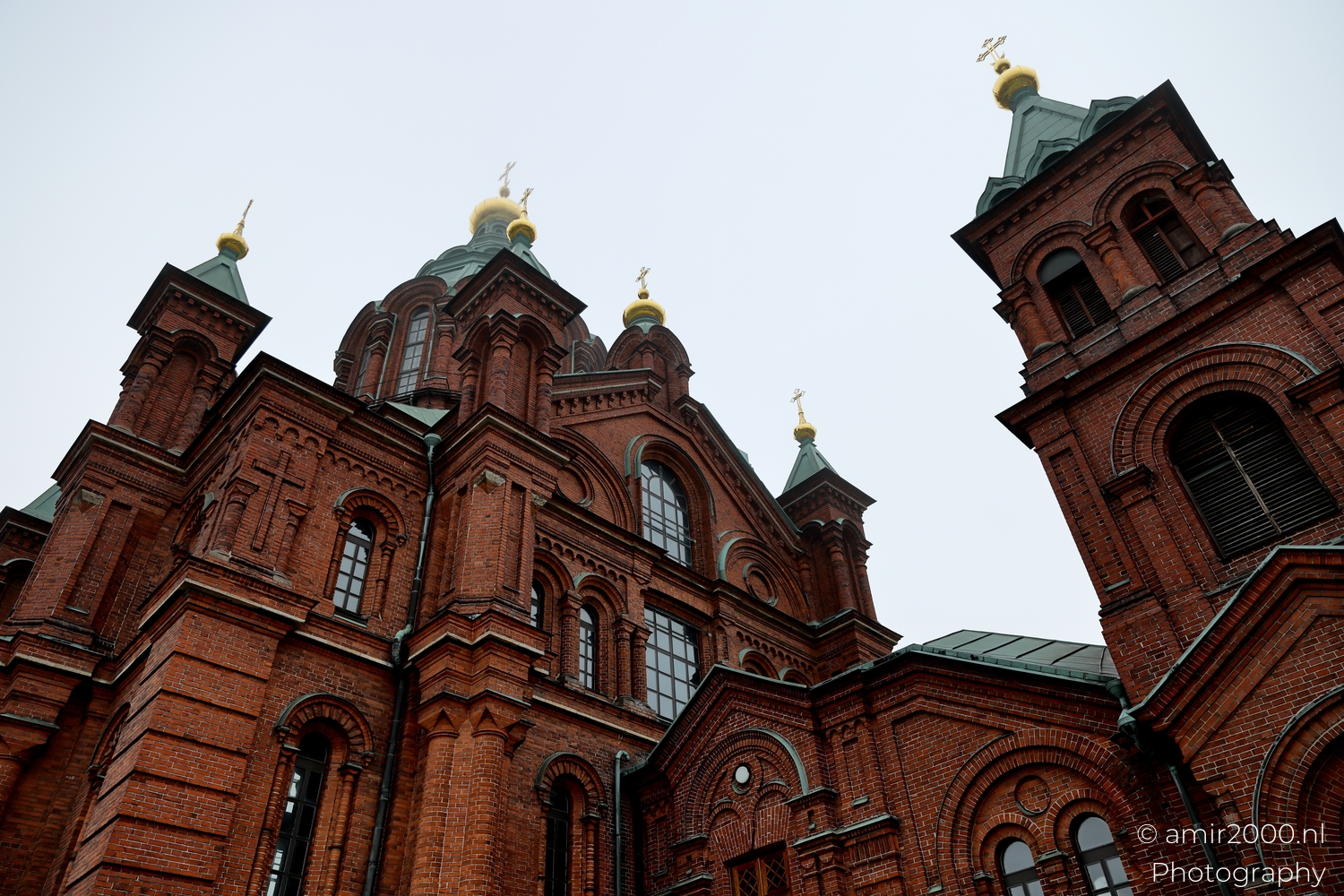 Uspenski Cathedral standing on a rocky hill with trees below and misty white sky above Helsinki waterfront.