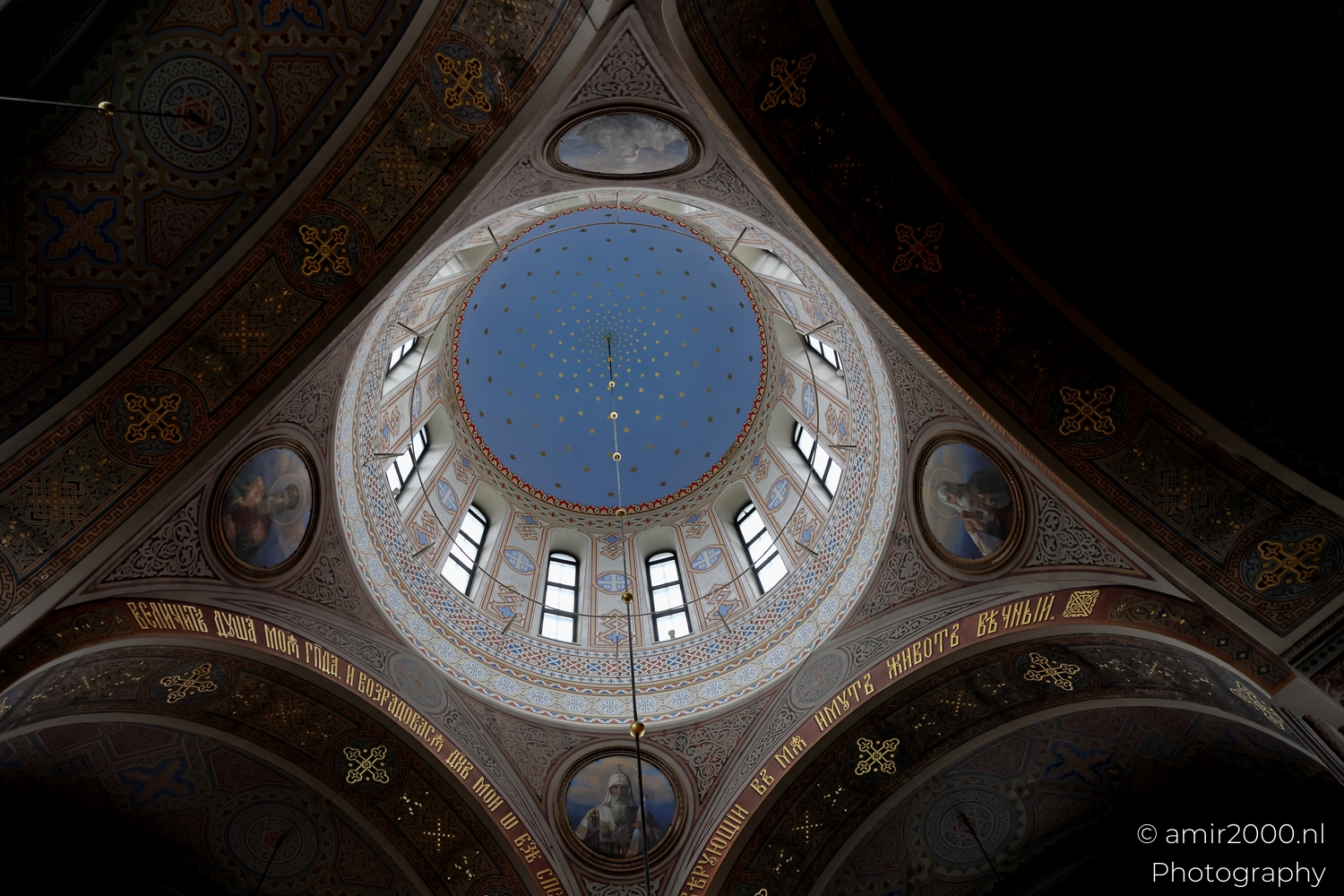 Painted dome of Uspenski Cathedral with blue ceiling gold stars and surrounding arches decorated with icons and patterns.