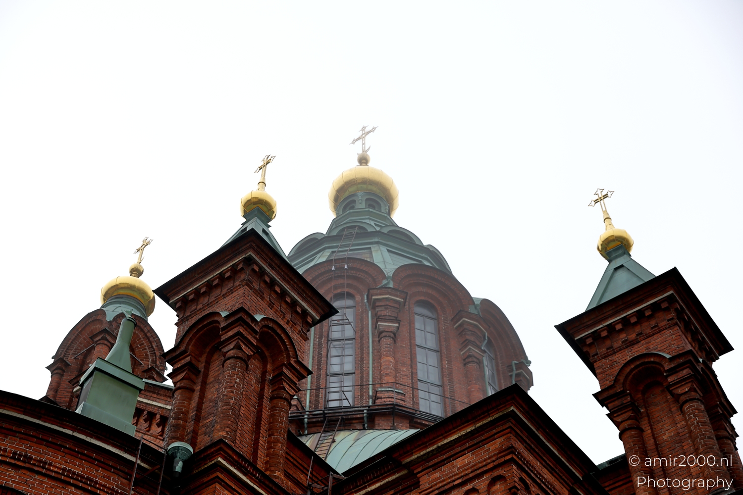 Low angle view of Uspenski Cathedral brick towers and arched windows rising sharply against a pale featureless sky.