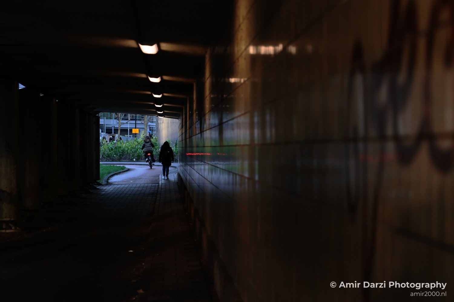 A dark urban passage illuminated by artificial lighting and adorned with graffiti on its walls in Amsterdam Netherlands.