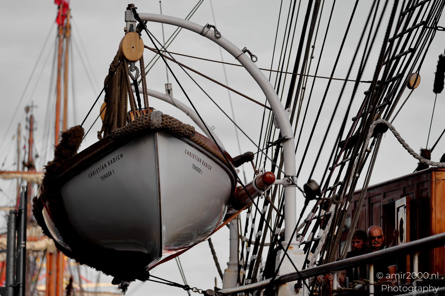 Christian Radich tender suspended in davits under overcast light with crossing rigging and wood pulleys