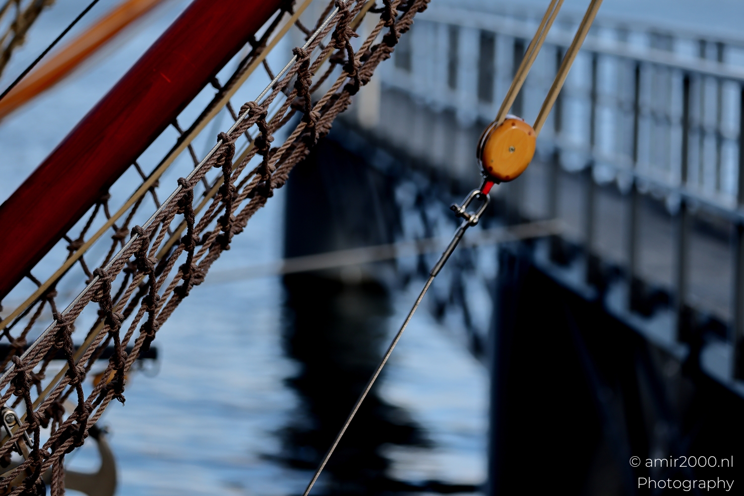Bowsprit netting with small block and a rope locked off near pier, shallow depth and harbor backdrop