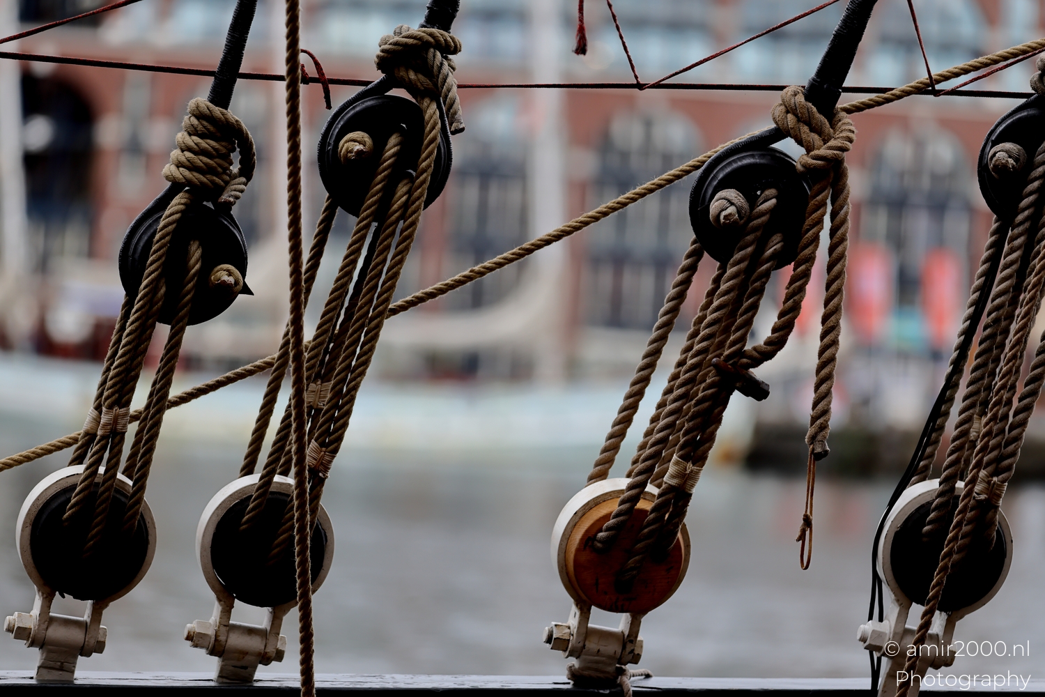 Row of deadeyes and tightened lanyards along the rail with repeating blocks and city waterfront bokeh