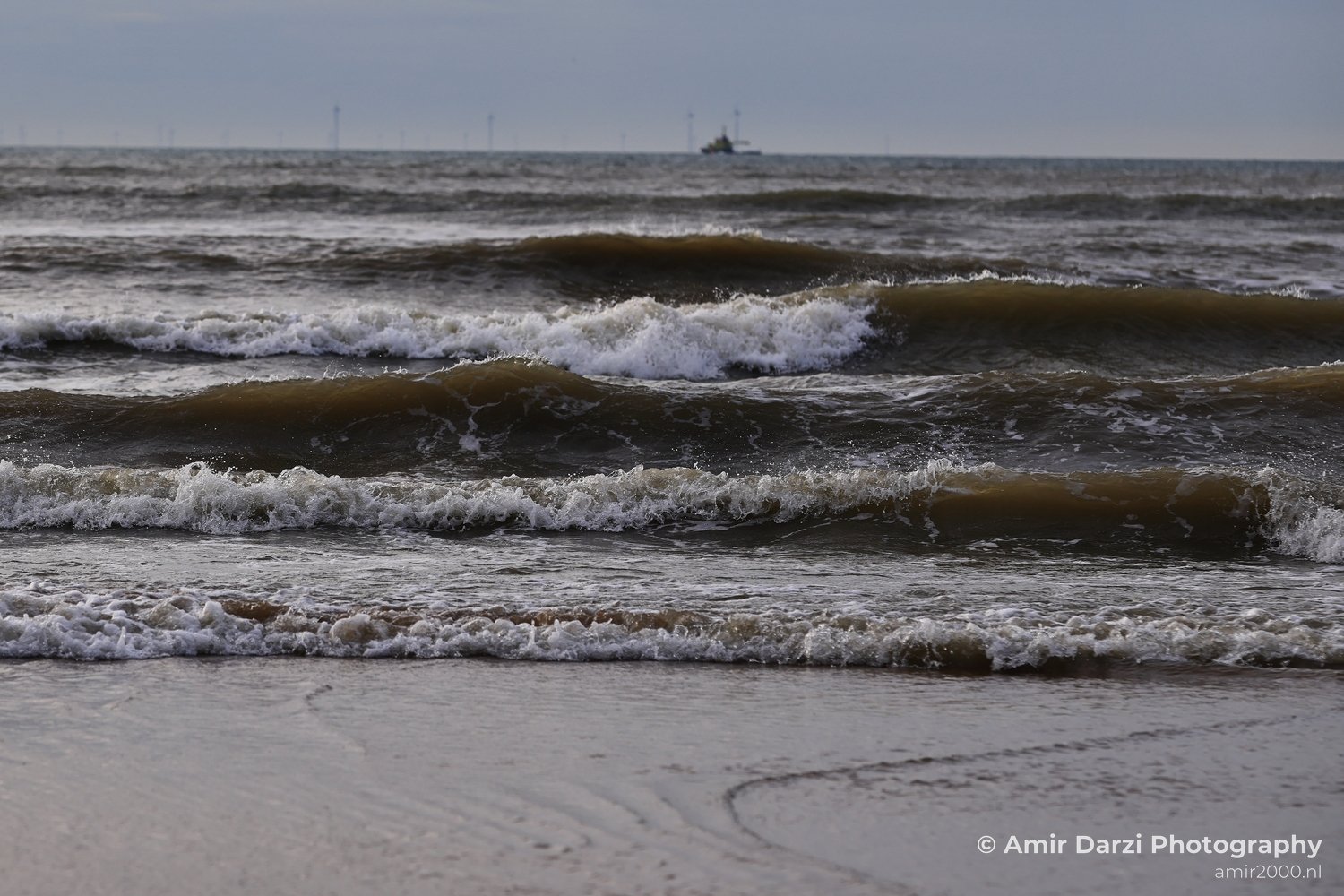 A tranquil coastal scene featuring waves near Zandvoort Netherlands during twilight and renewable energy infrastructure in the distance.